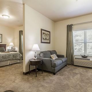 A cozy apartment with a small living area, featuring a sofa and lamp, adjacent to a bedroom.