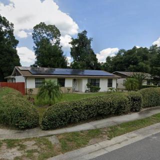 A suburban house with solar panels on the roof, surrounded by greenery and trees.
