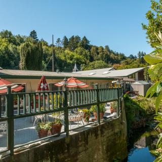 A charming restaurant with outdoor seating overlooking a waterway, surrounded by lush greenery on a sunny day.