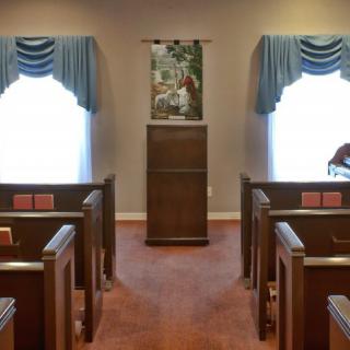 A small chapel interior with wooden pews and a central pulpit.
