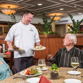 A waiter serves a meal to a senior couple in a restaurant setting.