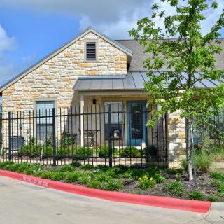 A charming house with a stone exterior, surrounded by a black metal fence and landscaped greenery.