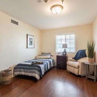 A cozy bedroom with a single bed, an armchair, and a nightstand under a window.