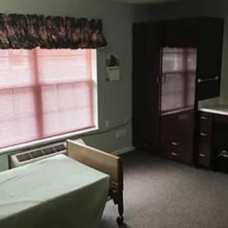 A simple bedroom with a bed, dresser, and large window with curtains.