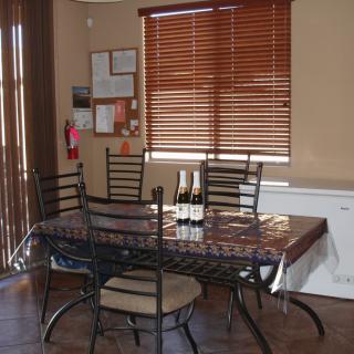 A dining room with a table and chairs, featuring wine bottles and window blinds.