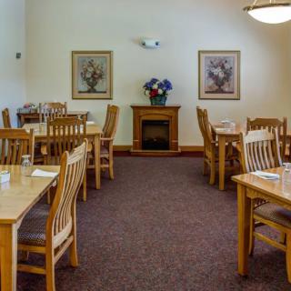 A cozy dining room with wooden tables and chairs, decorated with framed art and a floral arrangement.