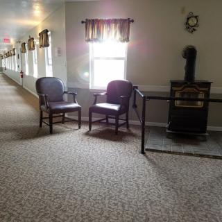 A quiet hallway featuring two chairs, a window with curtains, and carpeted flooring.