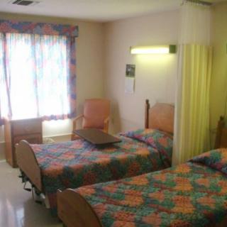 A hospital room with two twin beds, separated by a curtain, and a window with colorful curtains.