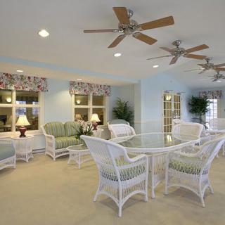 A spacious living room featuring rattan furniture, ceiling fans, and ample natural lighting.