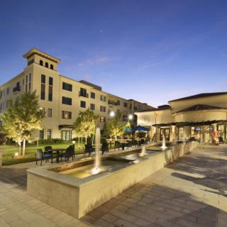 Evening view of a beautifully lit building with fountains and trees.