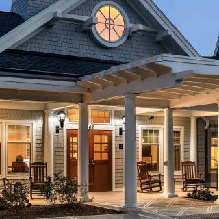 A charming house with a lit porch and inviting seating area in the evening.