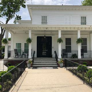 A white house with a porch and columns, featuring hanging plants and an inviting entrance.