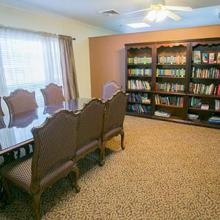 A cozy library and meeting room featuring a large table, chairs, and wall-to-wall bookshelves filled with books.