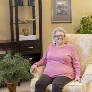 An elderly woman sitting comfortably in an armchair in a cozy living room setting.