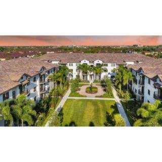 Aerial view of a residential building complex with landscaped gardens and palm trees under a sunset sky.