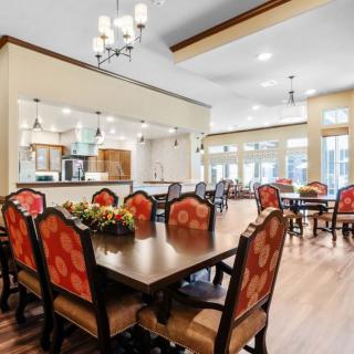 A spacious dining area with elegant decor, featuring wooden floors, chandeliers, and a large table surrounded by ornate chairs.