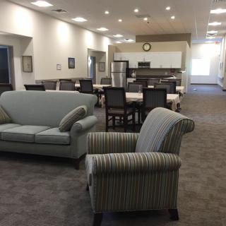 A spacious living area featuring a sofa, armchair, dining table, and a kitchen in the background.