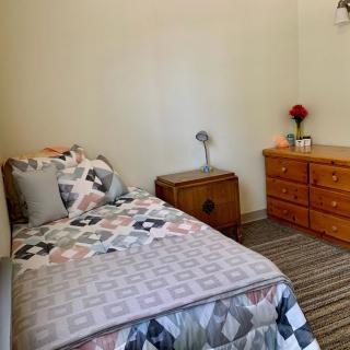A cozy bedroom with a single bed, quilt, dresser, lamp, and rug.