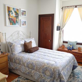 A cozy bedroom with a neatly made bed, decorative artwork, and warm natural lighting.