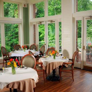 An elegant restaurant dining room with beautifully set tables and large windows offering natural light.