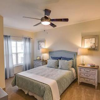 A cozy bedroom with a neatly made bed, soft blue and white decor, two nightstands with lamps, and a ceiling fan.