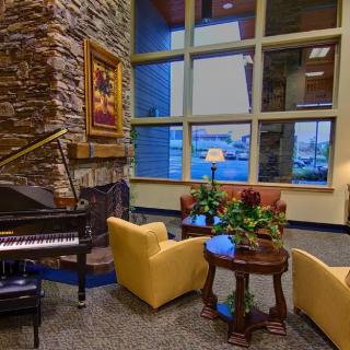 A cozy lobby interior with a grand piano, fireplace, armchairs, and large windows.