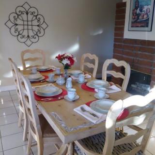 A dining table set for a meal, adorned with plates, cutlery, and a vase of flowers, illuminated by natural sunlight.