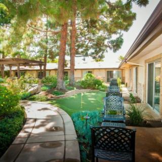 A serene garden with a winding pathway, outdoor seating, and lush greenery basking in sunlight.