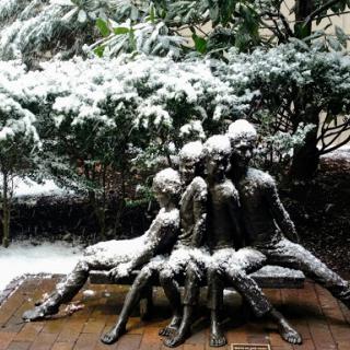 A beautiful sculpture of four children sitting on a bench, gently dusted with snow.