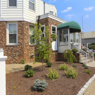 A residential house with brick exterior, landscaped garden, and a green awning over the porch.