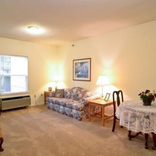 A cozy living room with a sofa, table, and lamps, featuring warm lighting and carpeted flooring.
