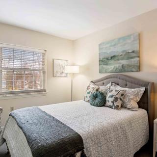 A cozy bedroom featuring a neatly made bed with decorative pillows, a standing lamp, and framed artwork on the walls.