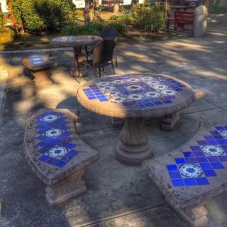 A decorative outdoor table and benches with blue mosaic patterns, set in a garden patio.