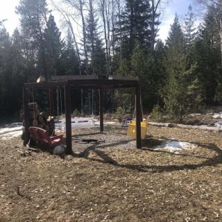 A small playground with swings surrounded by a forest on a sunny day.