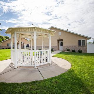 A white gazebo situated in a well-maintained yard with a house in the background on a sunny day.