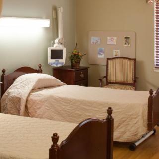 A hospital room with two beds, a chair, and a medical monitor.