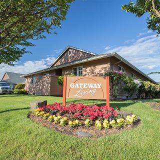 A house with a well-maintained lawn and a sign reading 'Gateway' surrounded by colorful flowers on a sunny day.