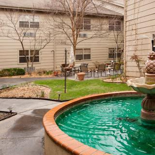 A serene courtyard featuring a central fountain surrounded by greenery and building structures.