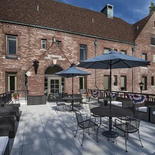 A sunny patio with tables, chairs, and umbrellas outside a brick building.