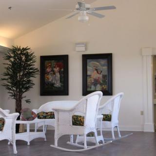 A cozy living room featuring white wicker furniture, an indoor plant, and framed artwork.
