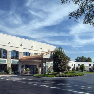 A commercial building with a parking lot and landscaped surroundings under a partly cloudy sky.