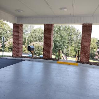 A view from an open parking area, showcasing brick columns and greenery in the background.