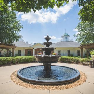 A beautiful outdoor fountain surrounded by greenery and architecture under a clear blue sky.