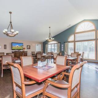 A spacious dining area with wooden tables and chairs, illuminated by chandeliers and abundant natural light from large windows.