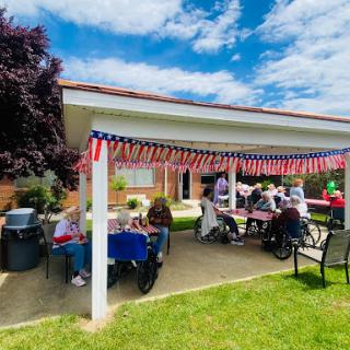 A lively community gathering under a decorated patio, filled with joyful conversations and summer sunshine.