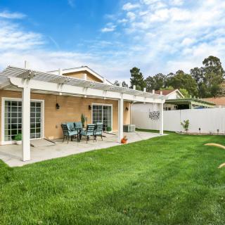 A backyard patio with a pergola overlooking a neatly maintained lawn and outdoor seating.