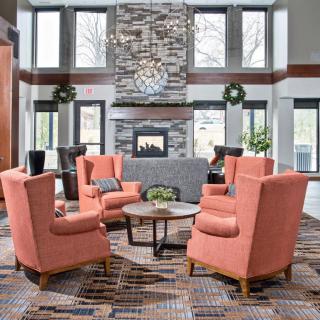 A modern lounge area with coral chairs surrounding a coffee table in front of a stone fireplace.