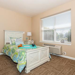 A cozy bedroom with a bed, colorful bedding, and a large window bringing in natural light.