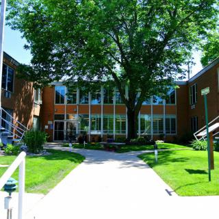 A modern building surrounded by lush greenery with a pathway leading to the entrance.