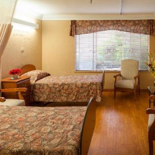 A cozy bedroom with two beds, an armchair, and a large window letting in natural light.